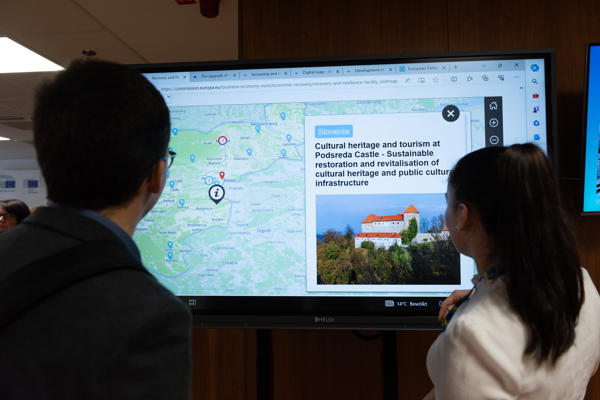 LEtna konferenca NOO (Foto: dva posameznika iz občinstva si na projekciji ogledujeta zemljevid slovenskih projektov NOO z izpostavljenim gradom Podsreda) 