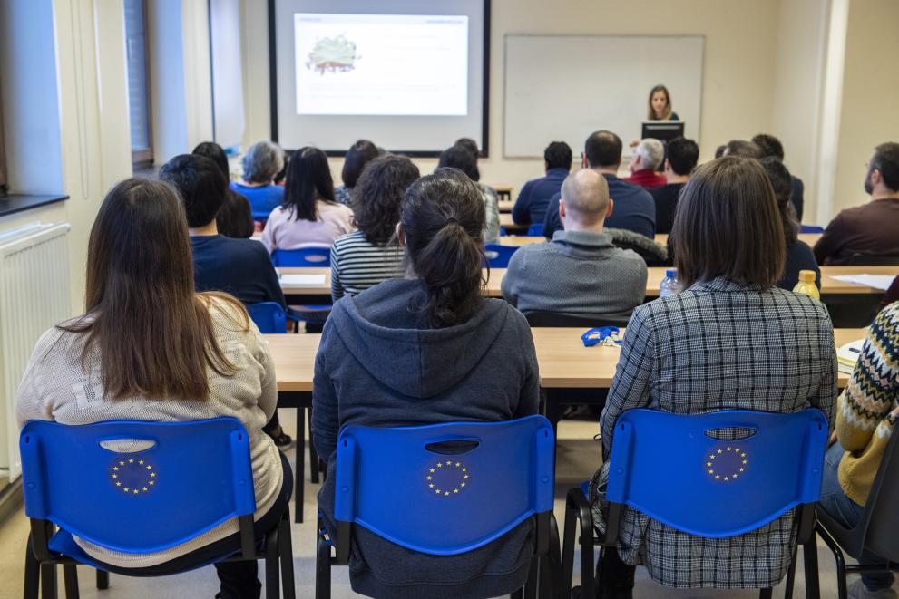 Mednarodni dan izobraževanja (Foto: poln razred dijakov ali študentov, ki sedijo na modrih stoliih z emblemom EU (zvezdicami) na hrbtni strani