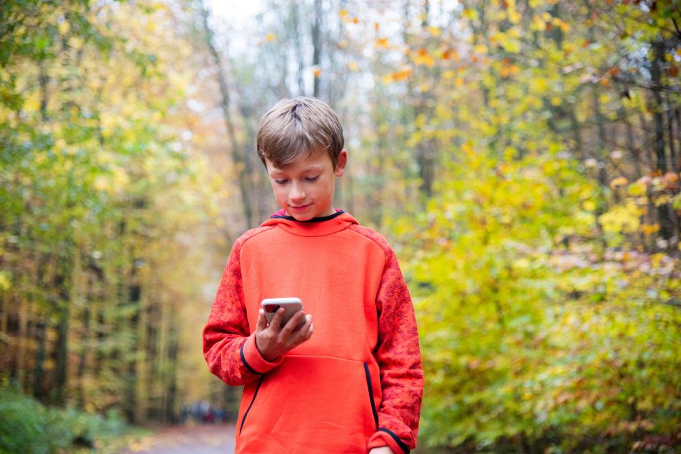 Uradni postopek zoper podjetje TikTok (Foto: Mlajši najstnik sredi gozda z nasmehom na obrazu gleda mobilni telefon)