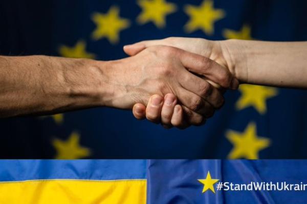 Instrument za Ukrajino (Foto: dve roki, ki se rokujeta z zastavo EU v ozadju in pasico v barvah ukrajinske zastava, na kateri je izpisan #StandWithUkraine)